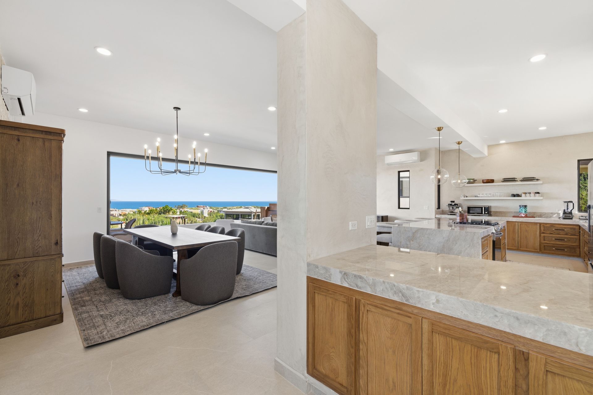 A bright, modern open-concept home with a dining area featuring ocean views and a kitchen with wood cabinetry and marble.