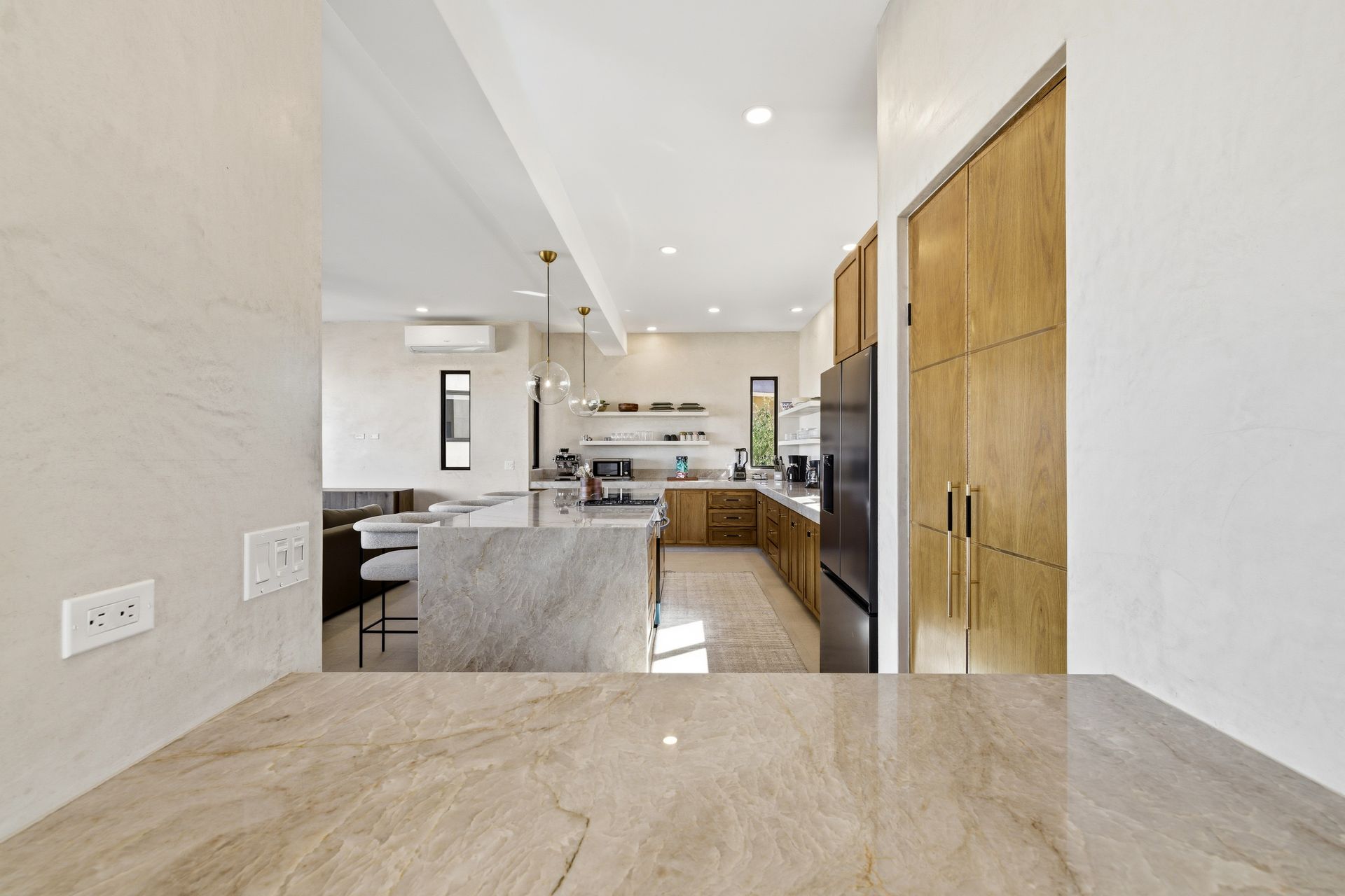 A modern, neutral-toned kitchen featuring a stone countertop foreground, a central island, and wood-paneled cabinetry.