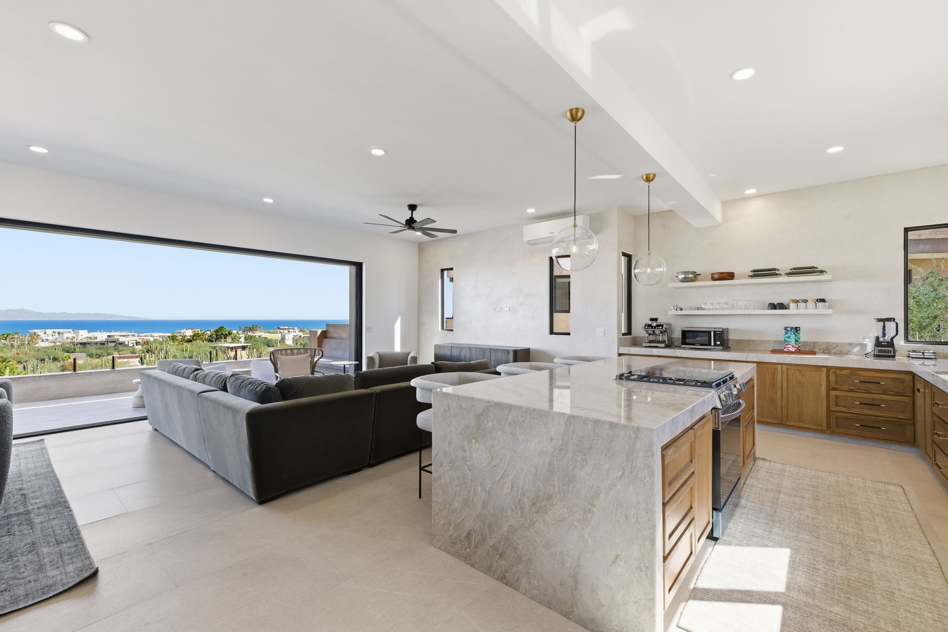An open-concept living area with a large island, wooden cabinets, and a wide sliding door overlooking the ocean.