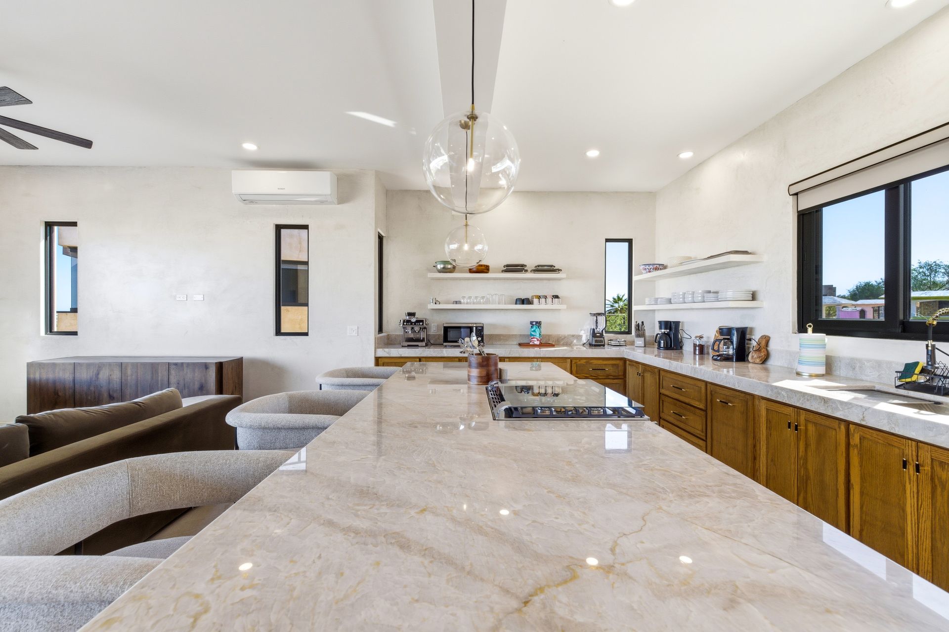 A kitchen interior with a large marble island, wood cabinets, a glass pendant light, and a sofa in the foreground.