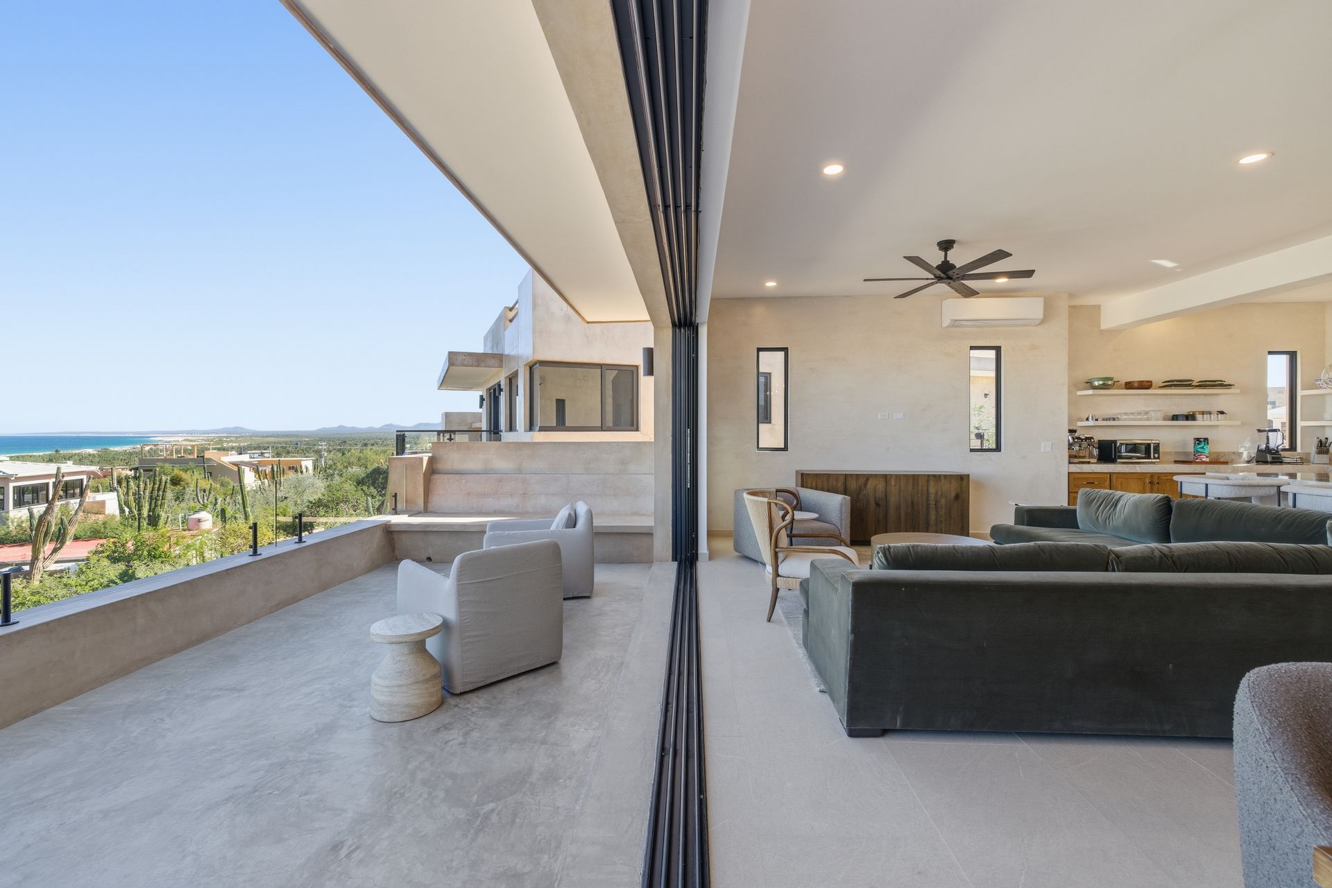Open-plan living room with large glass doors leading to a terrace overlooking a lush landscape and the distant sea.