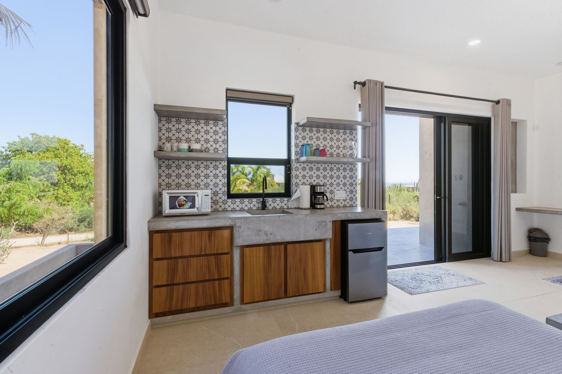 A kitchen kitchenette with wood cabinets, concrete countertop, microwave, and patterned tile backsplash in a room.