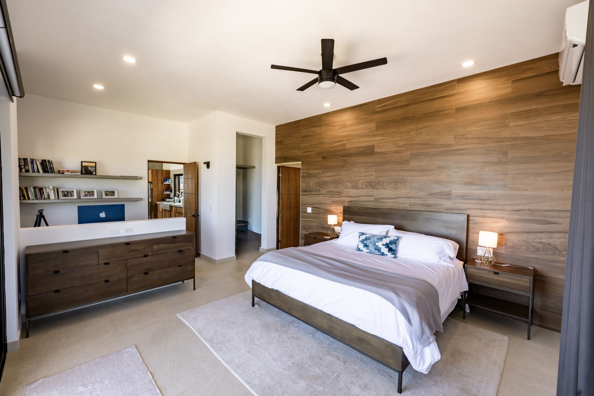 A spacious bedroom featuring a large bed with a wood-paneled accent wall, a matching dresser, and a ceiling fan.