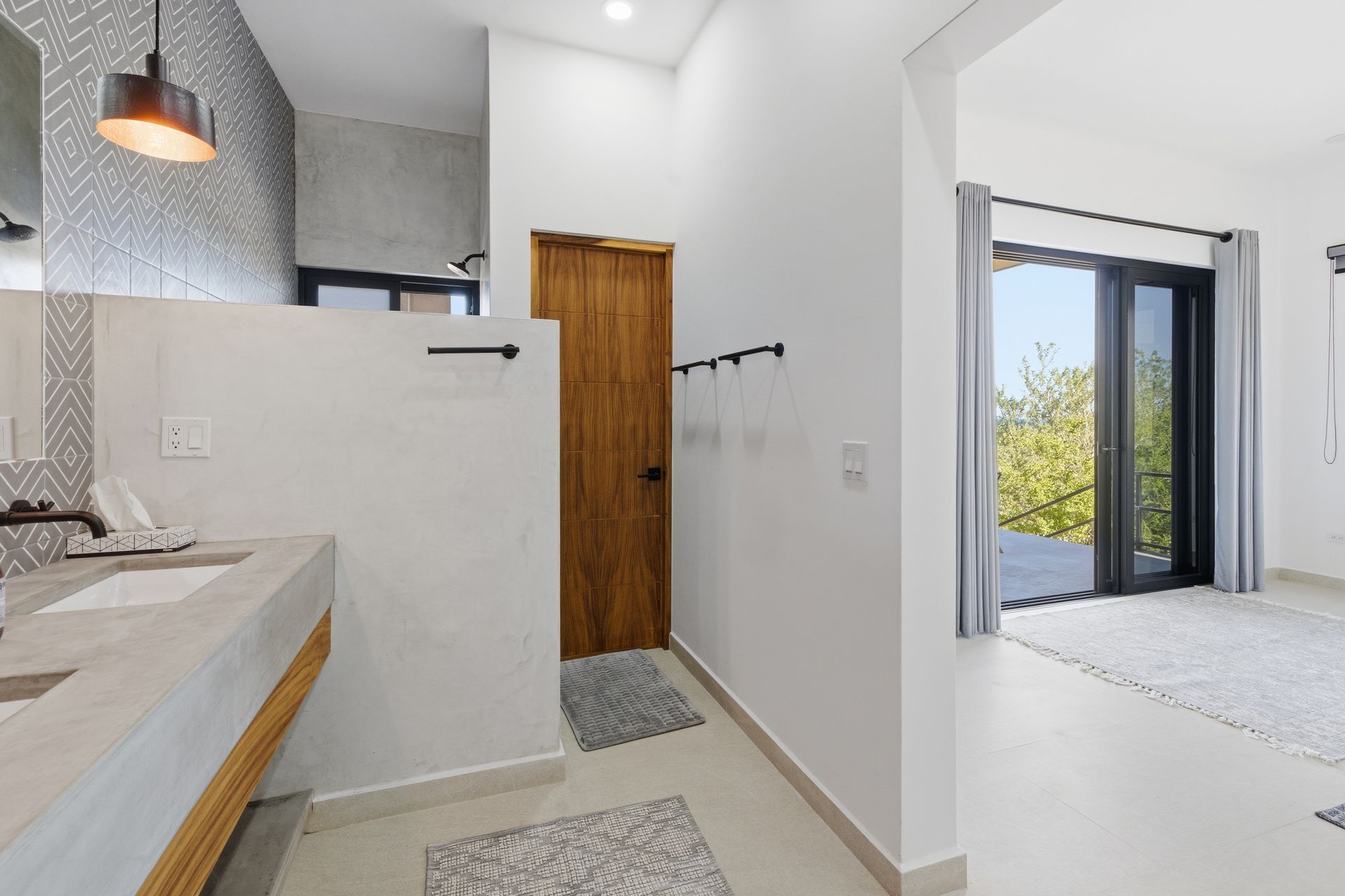 Bathroom with concrete sink, wooden door, and doorway to a bedroom with large windows.