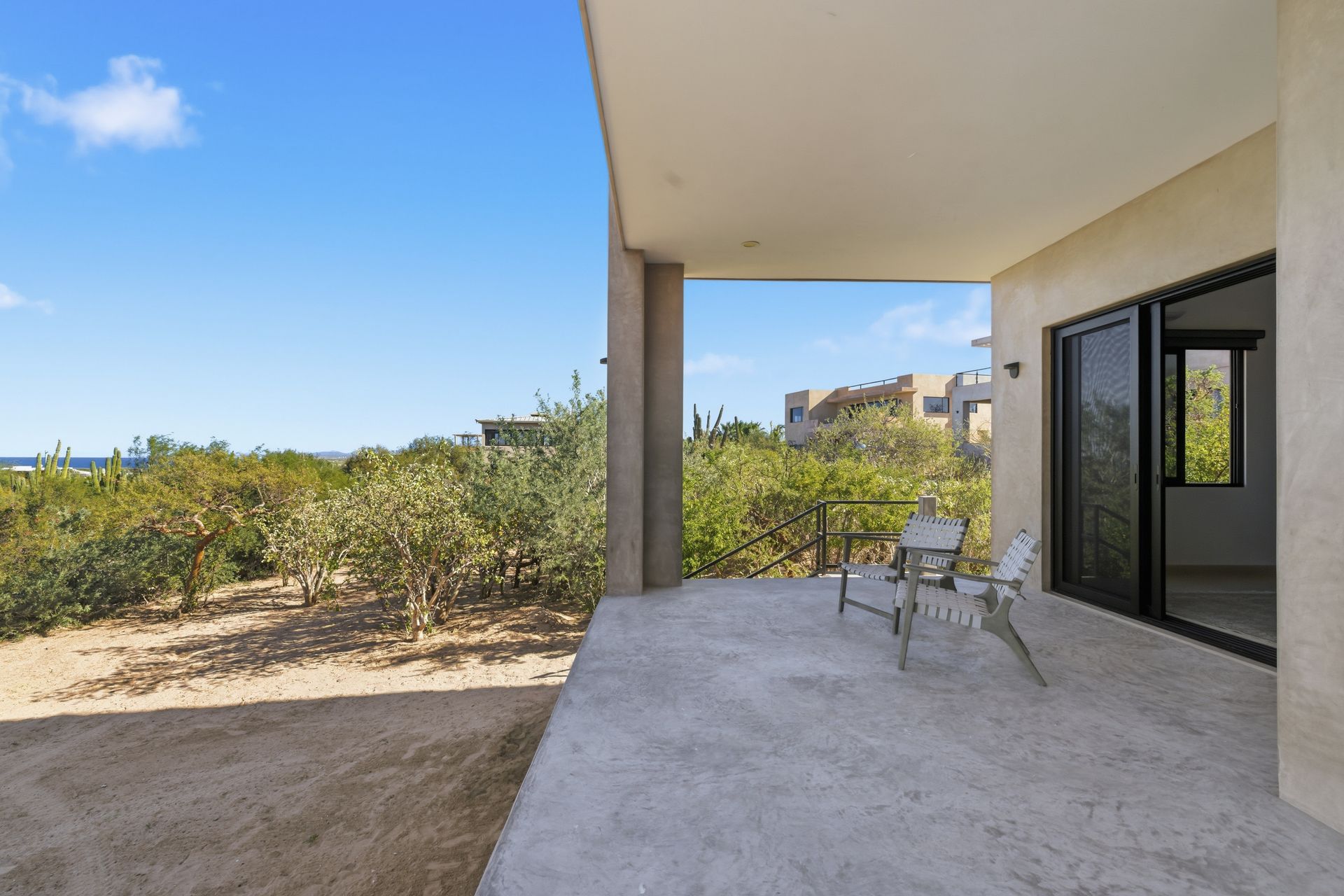A covered concrete patio with two chairs overlooking a dry landscape and distant buildings under a clear blue sky.