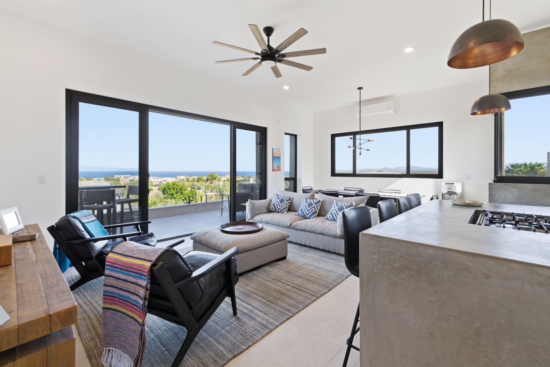 A bright, modern open-plan living room with a neutral color palette, sea view, and large sliding glass doors to a balcony.