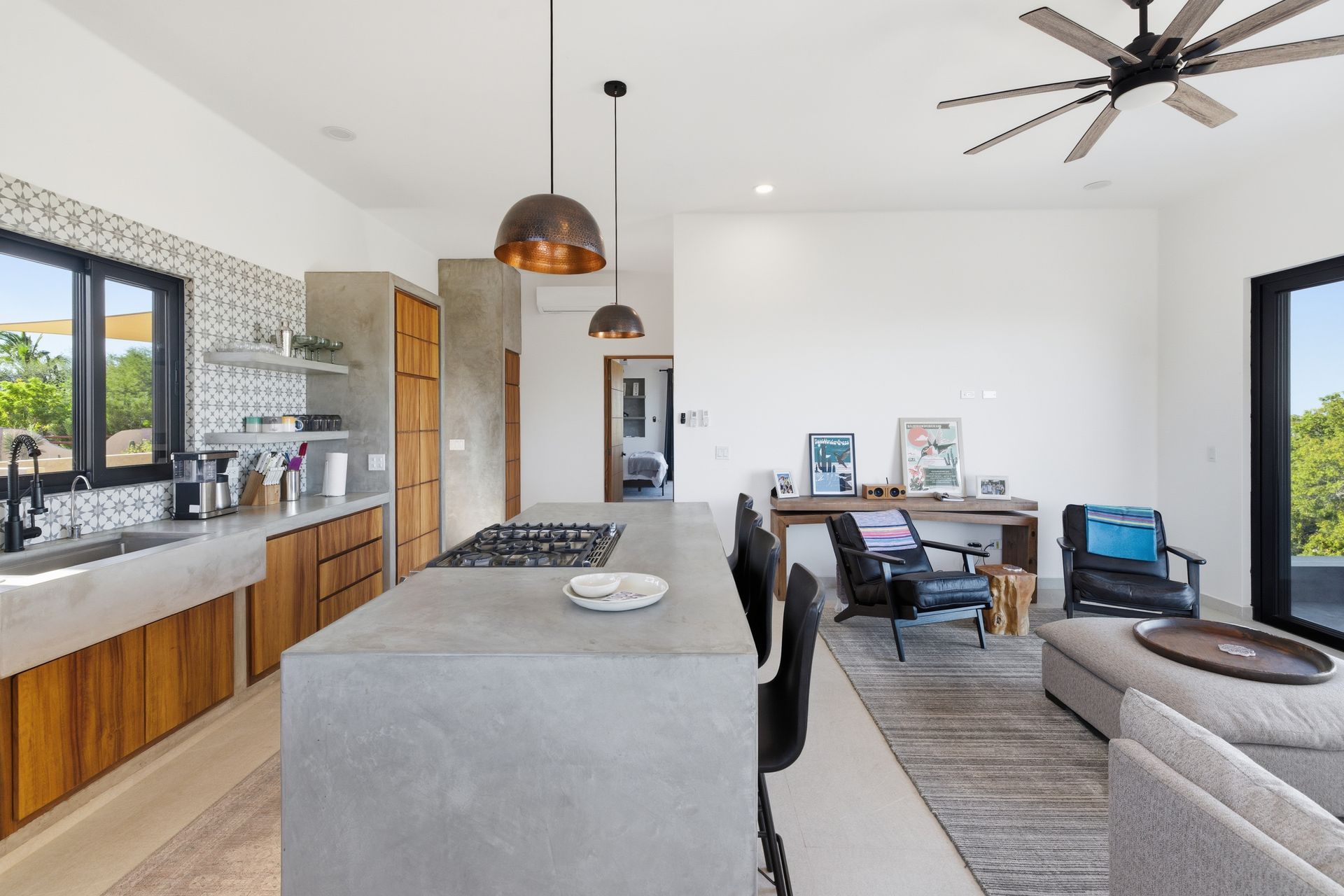 Modern open-plan kitchen with concrete island and counters, wooden cabinets, and a living area with armchairs and rug.
