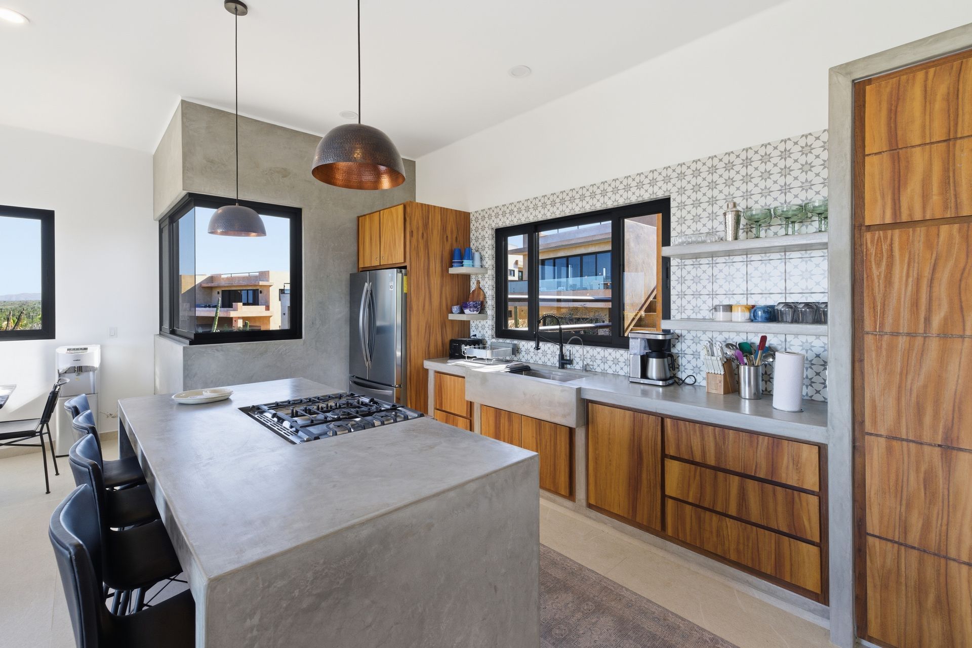 Modern kitchen featuring a large concrete island, wooden cabinets, patterned tile backsplash, and two pendant lights.