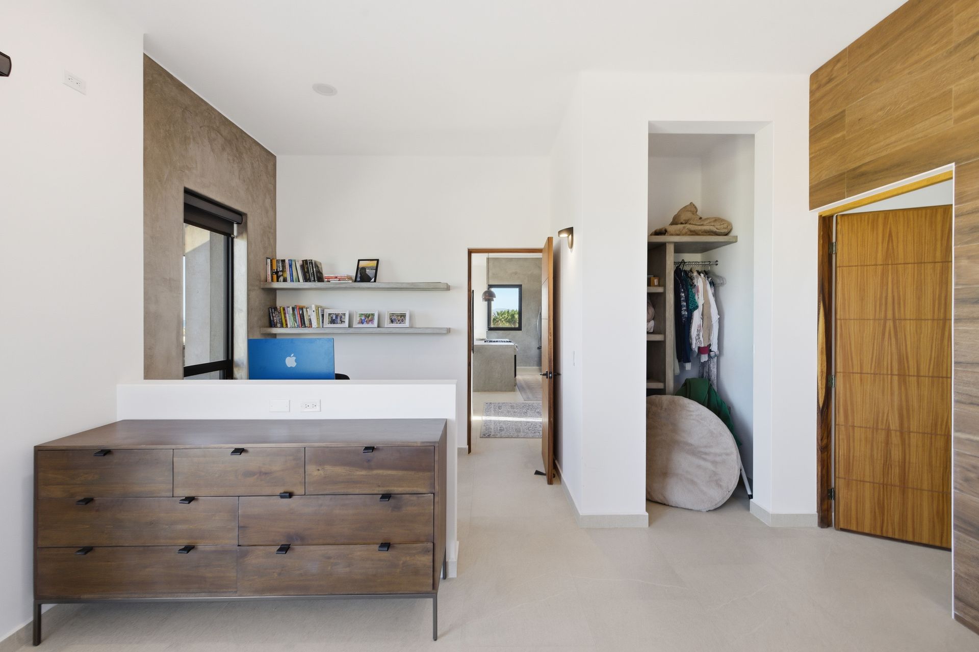 Modern home interior featuring a wooden dresser, shelves with decor, an open walk-in closet, and a light-wood door.