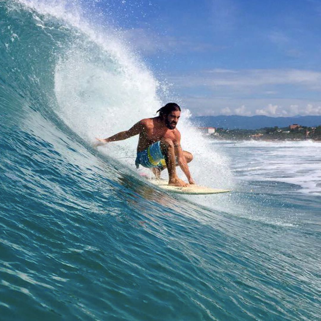 Man surfing a blue wave, arms outstretched, sunny beach.