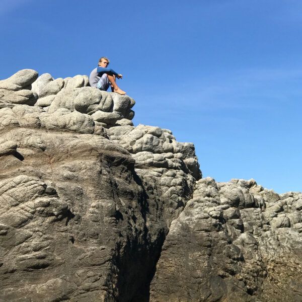 Person sits on rocky outcrop, gazing at blue sky.