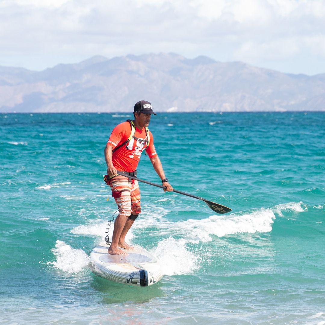 Man on a paddleboard in turquoise water; mountains in background.
