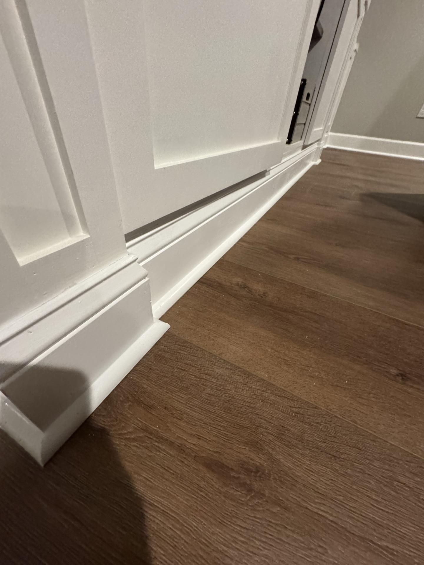 A close-up view of white floor trim or baseboards meeting dark brown wood-look flooring in a room.