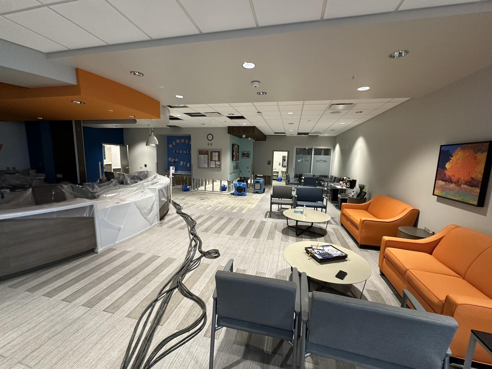 A waiting area under renovation with plastic-covered furniture, orange seating, and exposed flooring cables.