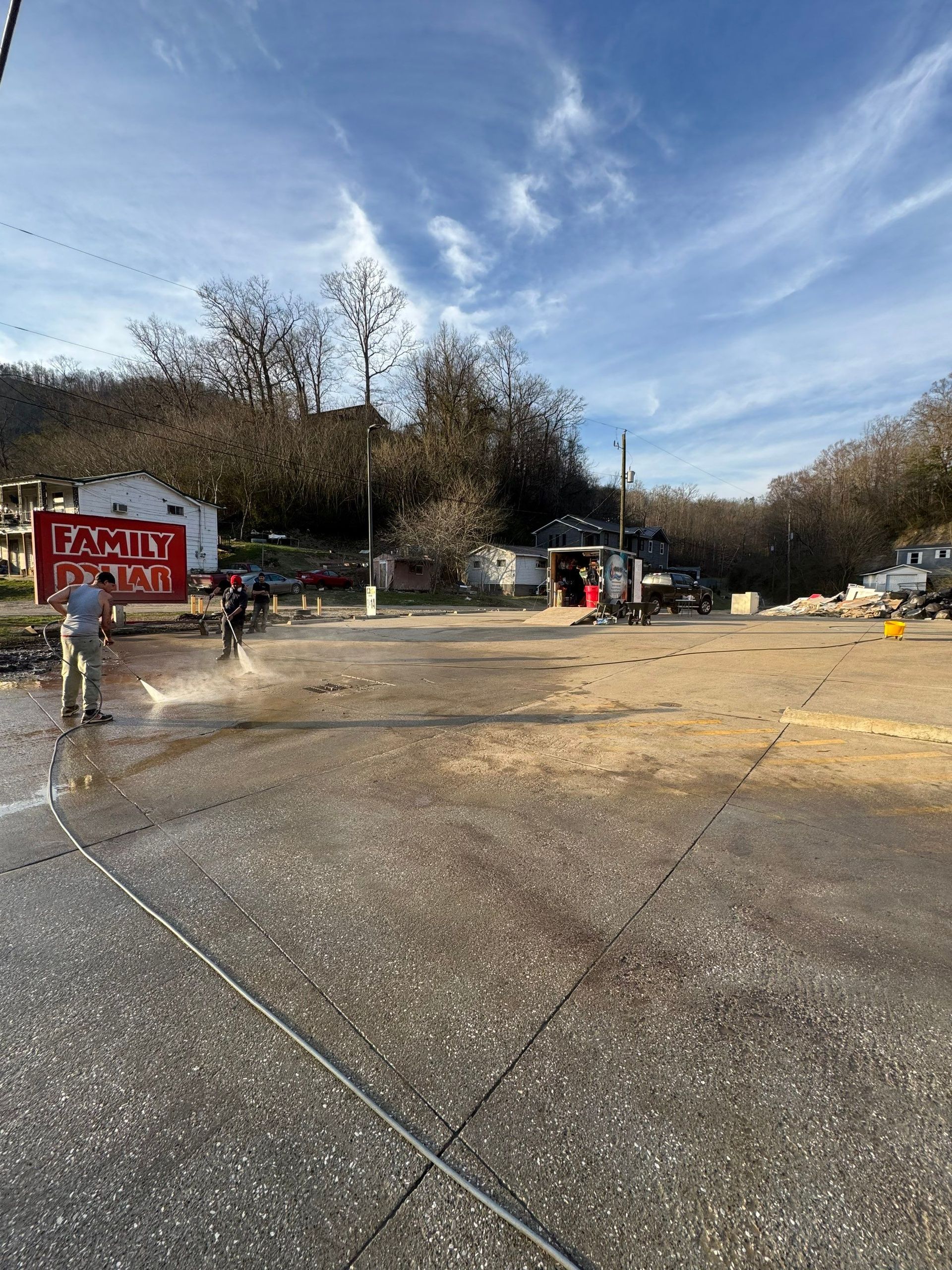 A person uses a hose to spray a large, gravel-filled outdoor space near a red 