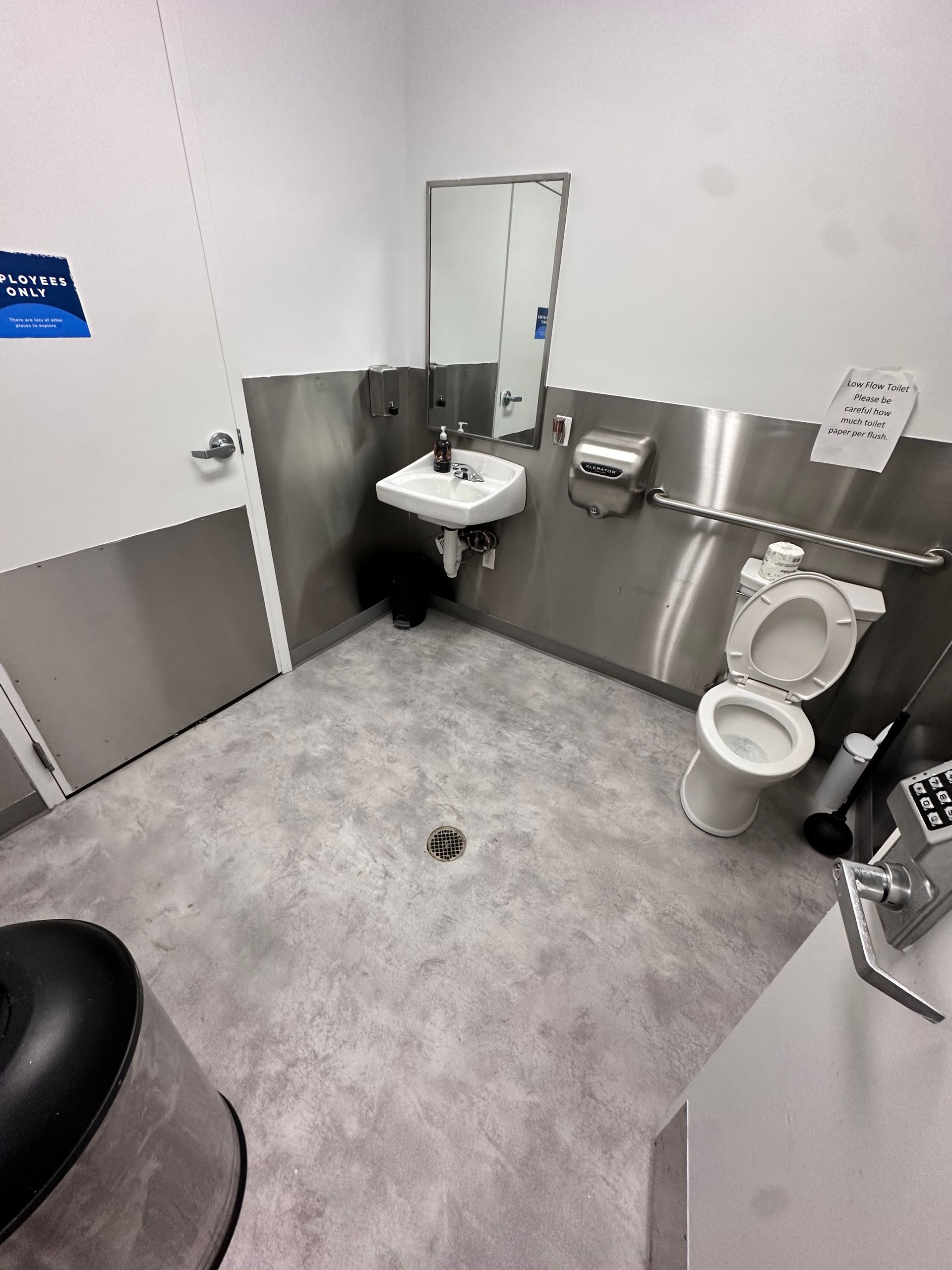 Accessible restroom with a toilet, grab bar, sink, mirror, and gray flooring.
