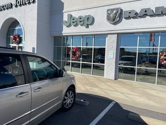 Silver minivan parked outside a Jeep dealership with storefront windows and signs visible