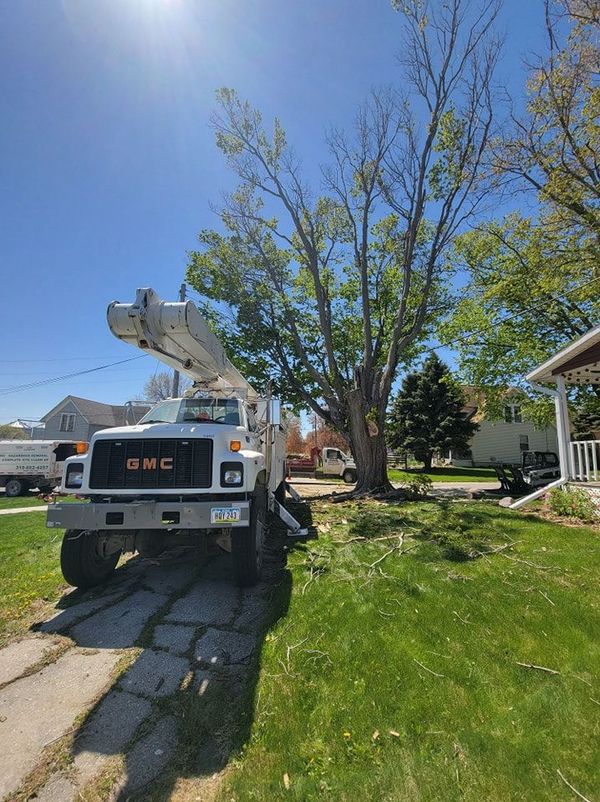 GMC utility truck with boom lift parked on a sunny suburban lawn near a house and large tree