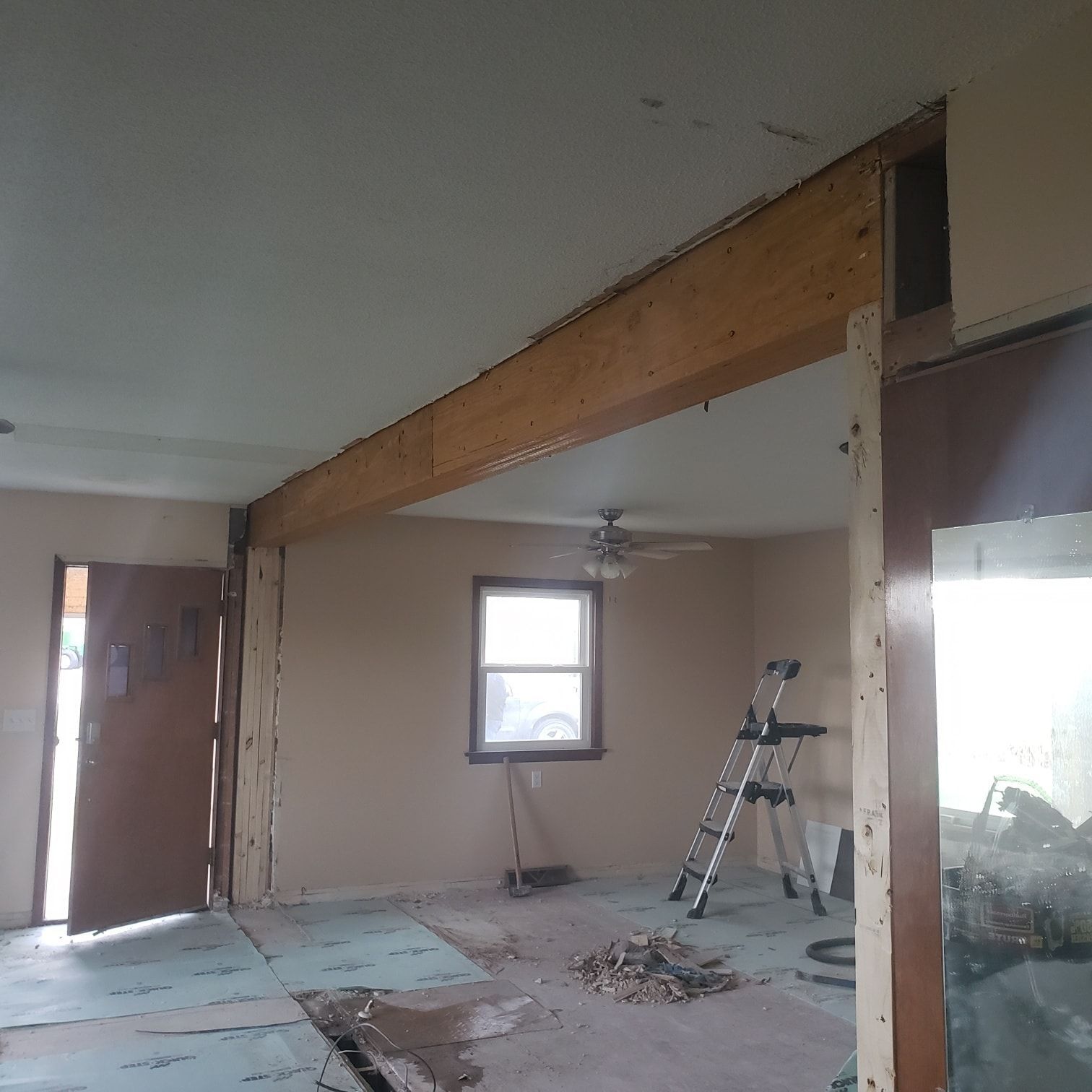 Partially renovated room with exposed beam, ladder, debris on floor, and a window.