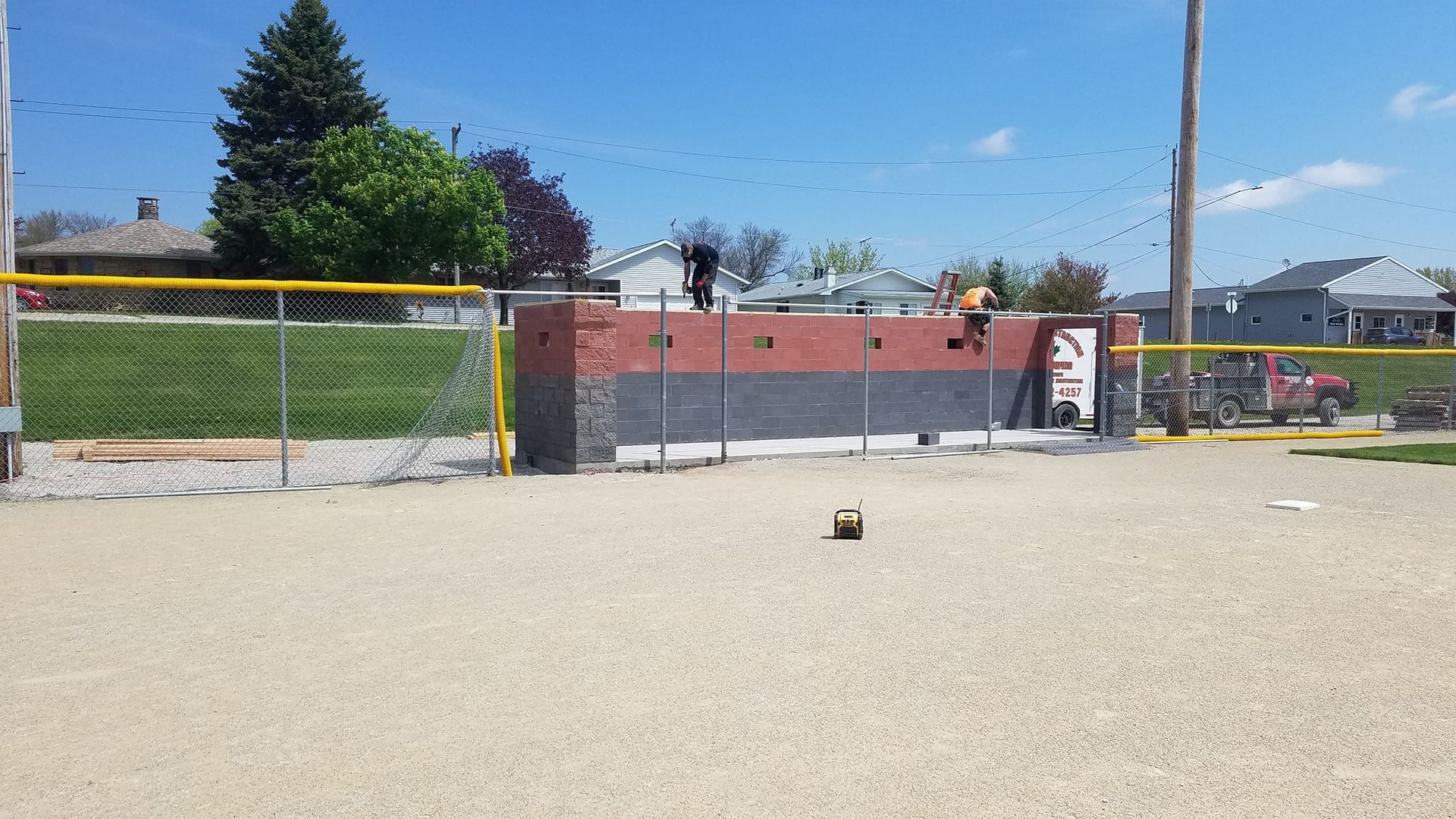Empty baseball field with chain-link fence, brick backstop, and scattered debris on the infield