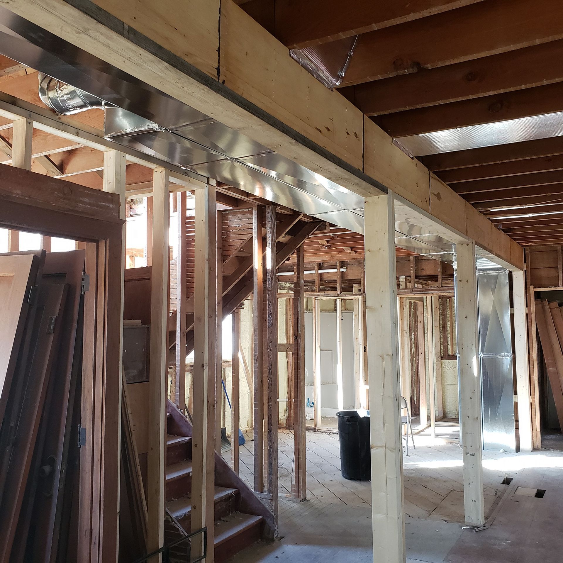 Exposed wooden framing and beams inside an unfinished house under construction, with open wall studs and stairway.