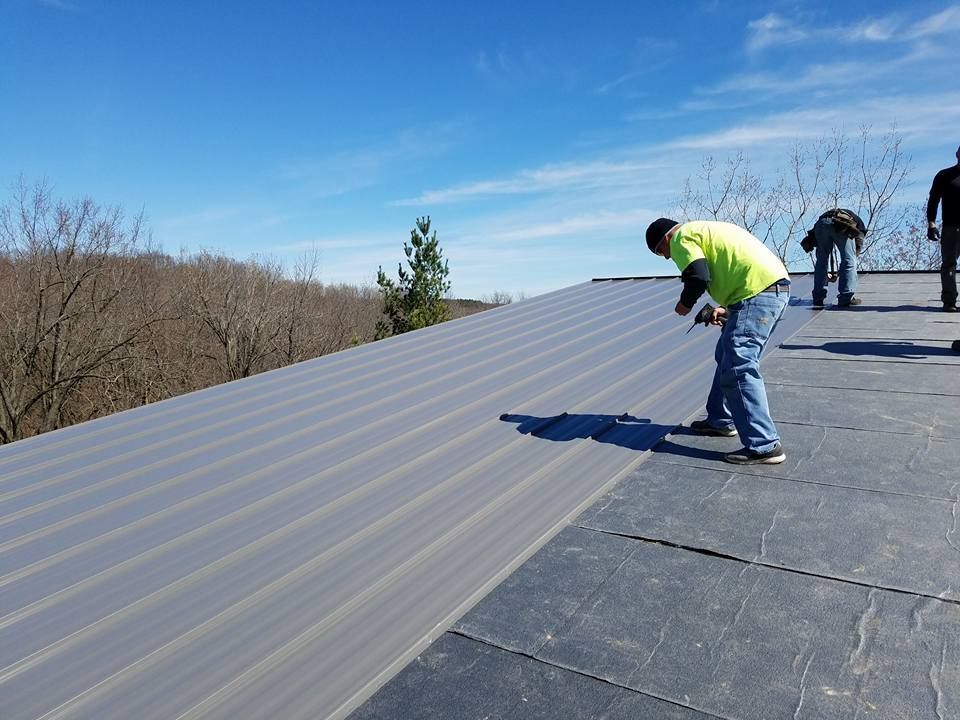 Workers installing metal roofing on a sloped roof on a clear day