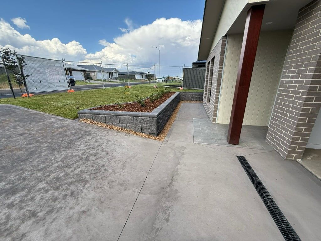 Concrete walkway next to a house with a raised garden bed, sunny day — Darlington Landscaping in Dubbo, NSW