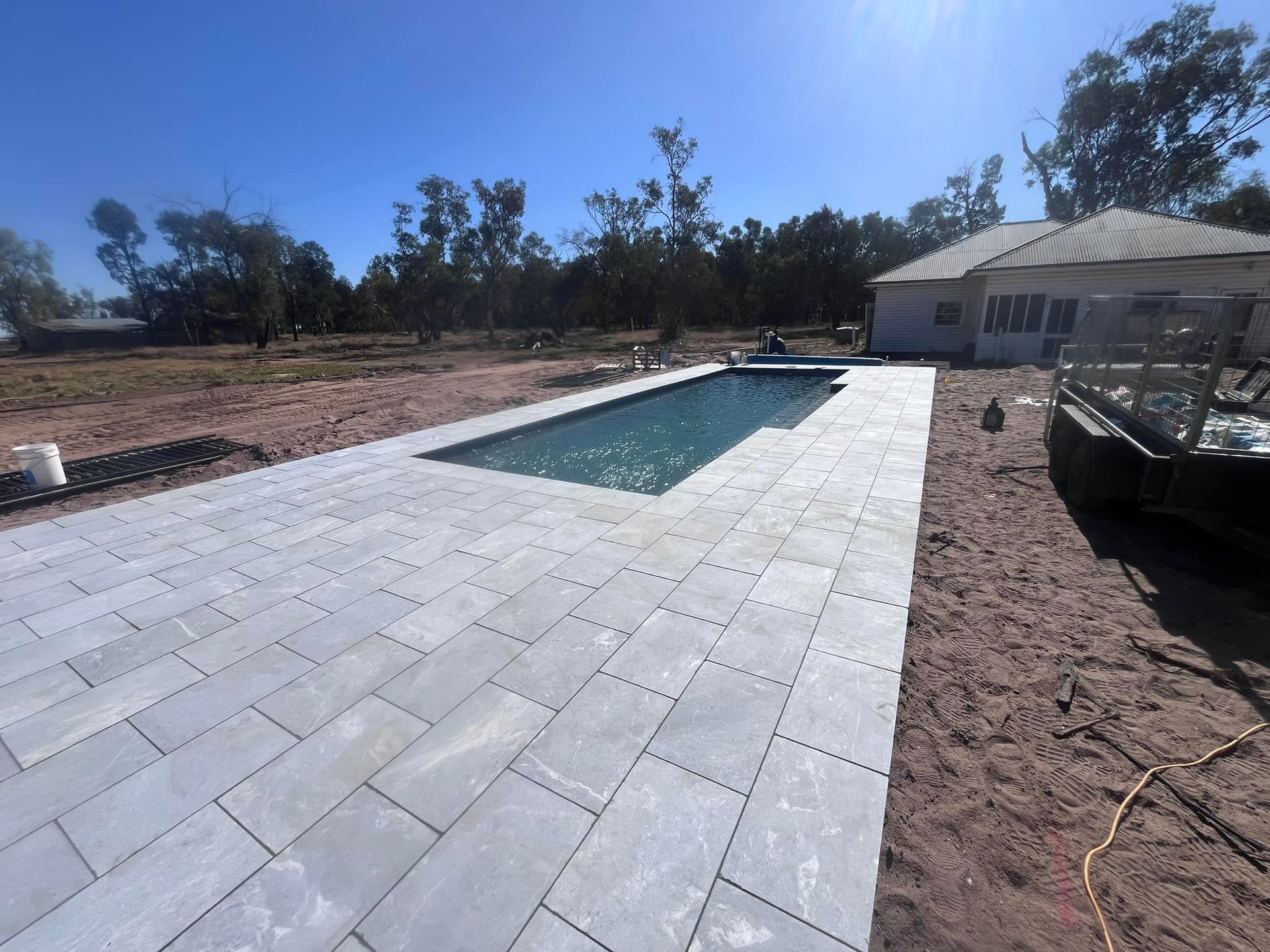 A rectangular pool with blue water is surrounded by grey paving. A house and trees are in the background — Darlington Landscaping in Dubbo, NSW