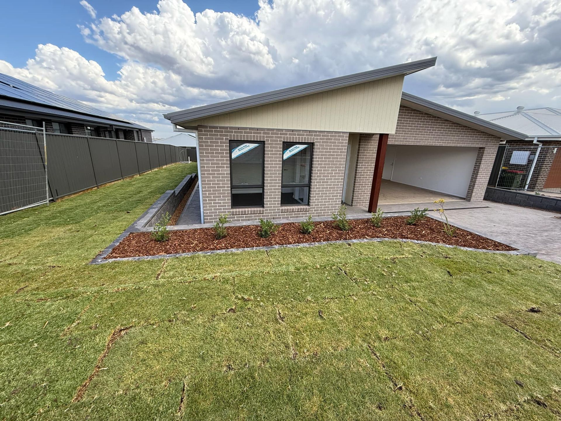 Modern brick house with sloping roof, garage, and landscaped front yard under blue sky — Darlington Landscaping in Dubbo, NSW