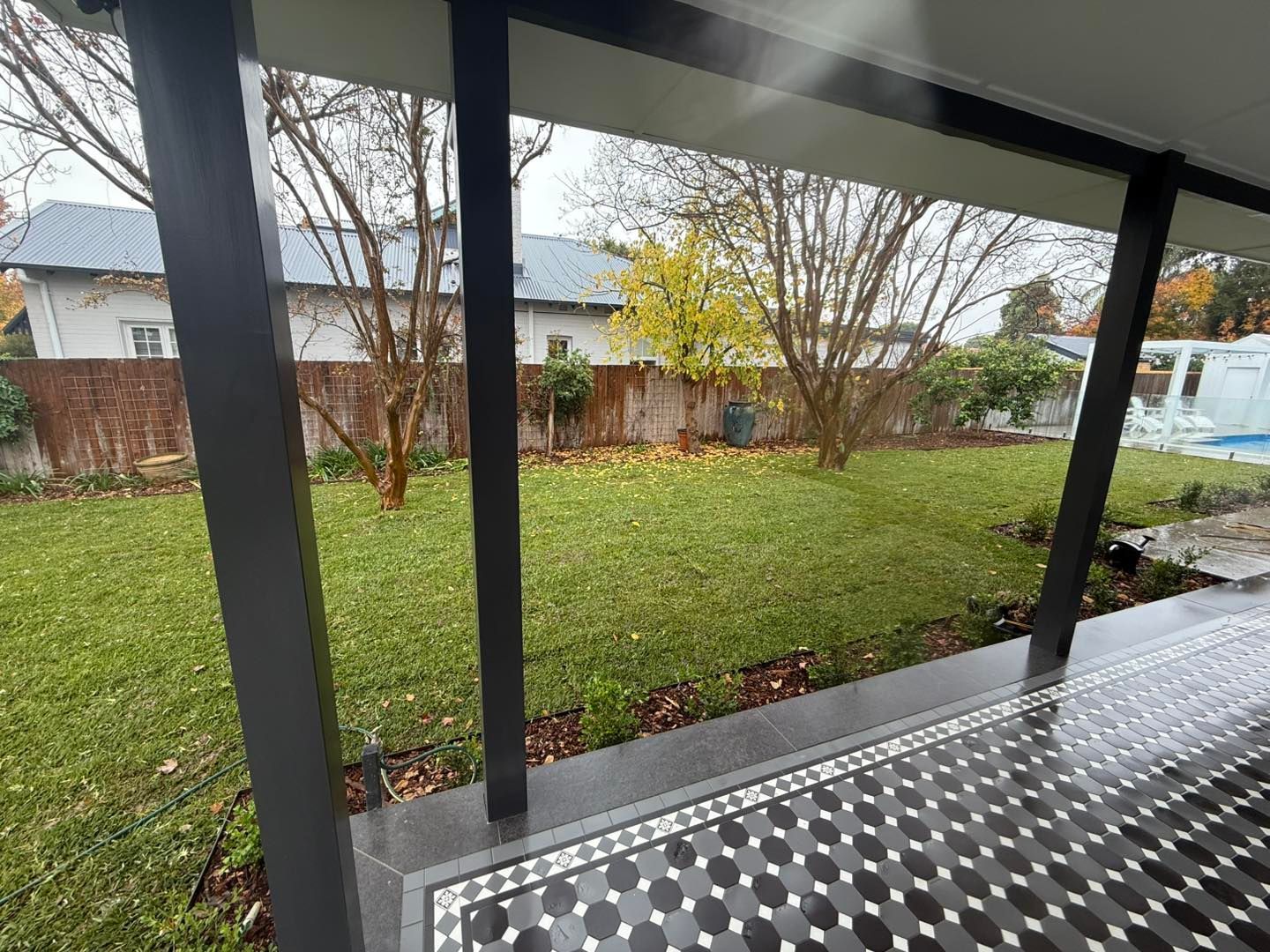 Lawn viewed from a porch, with trees, houses, and patterned floor. Grey and black colours — Darlington Landscaping in Dubbo, NSW