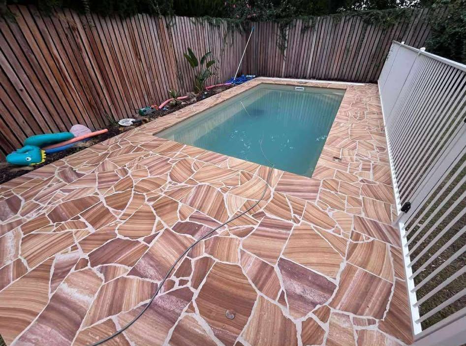 A rectangular swimming pool surrounded by stone pavers. A building is to the right and a brown wall to the left — Darlington Landscaping in Parkes, NSW