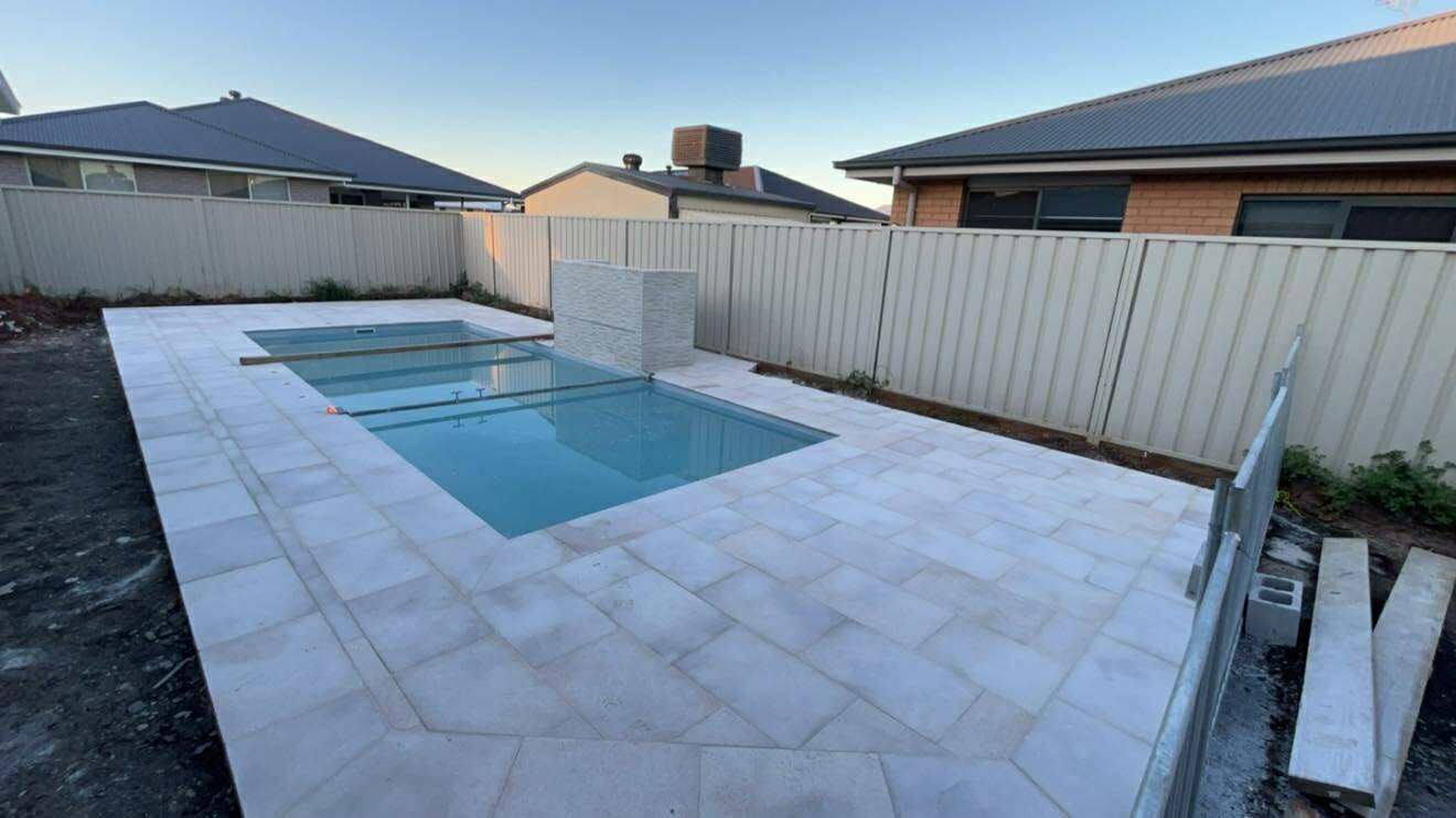 Backyard pool with light gray tile, fenced area, houses in the background — Darlington Landscaping in Narromine, NSW