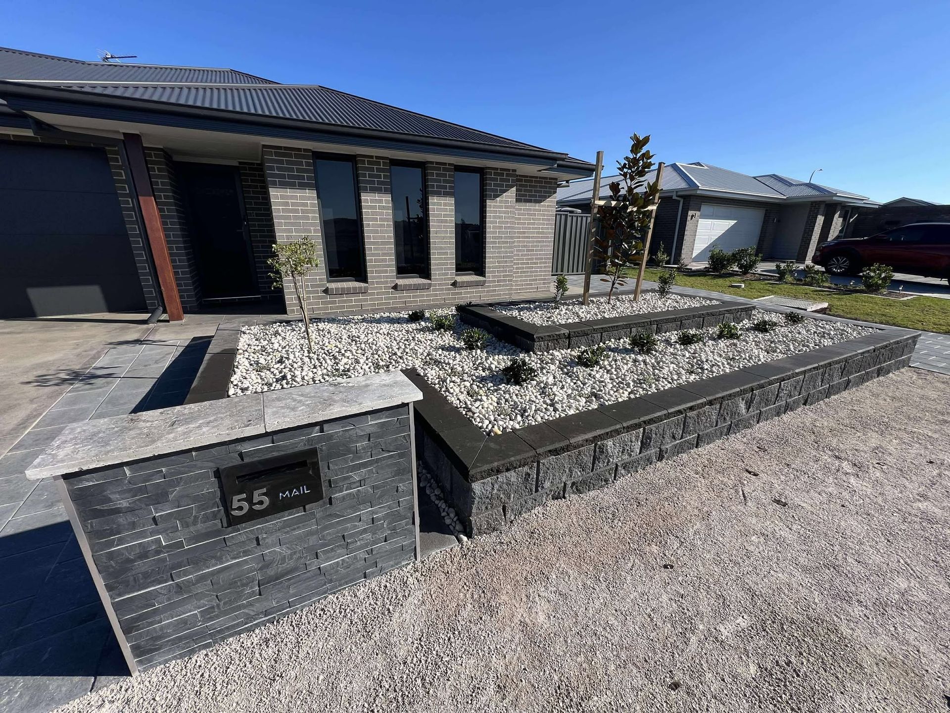 Modern home with landscaped front yard; black brick, raised garden beds with white stones, grry driveway — Darlington Landscaping in Narromine, NSW