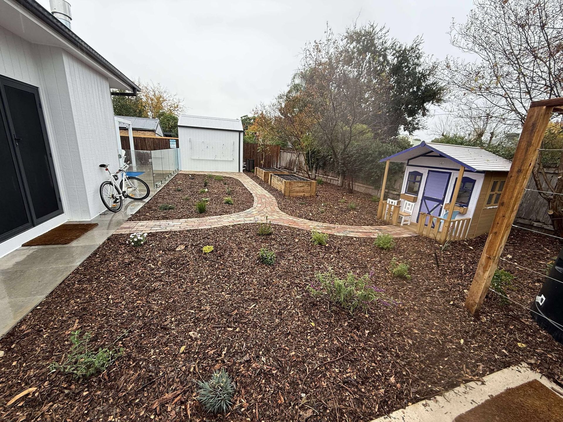Backyard with a mulched garden, brick pathways and a playhouse — Darlington Landscaping in Wellington, NSW