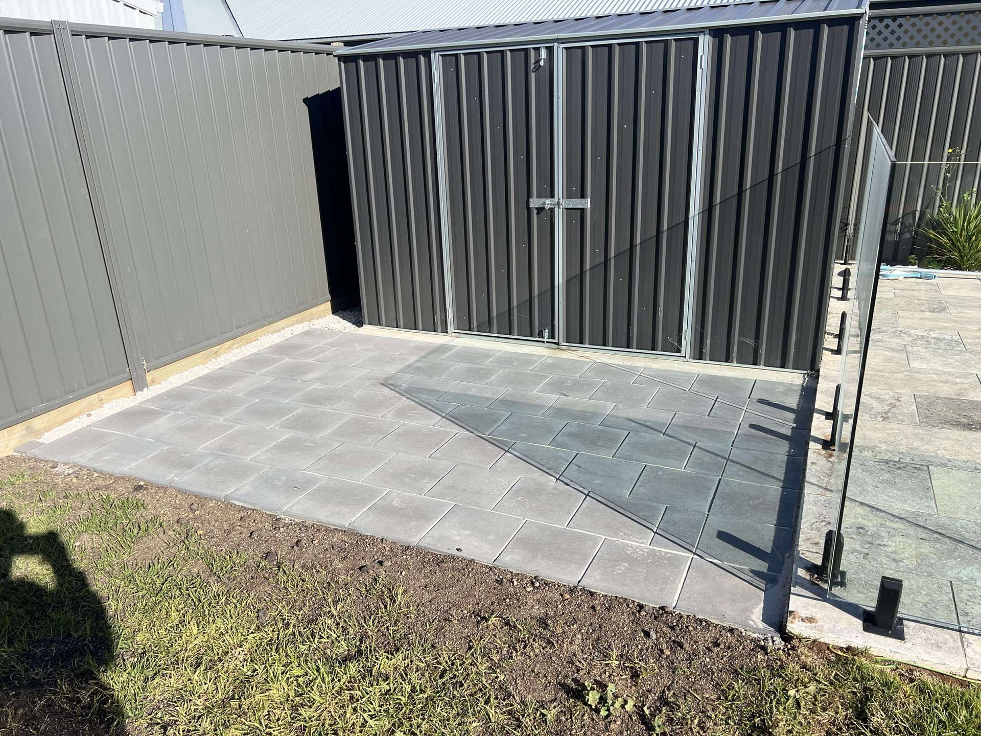 Gray shed with tiled patio in a backyard, next to a fence and grass — Darlington Landscaping in Narromine, NSW