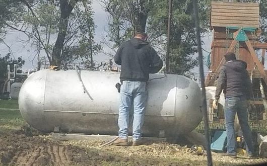 Two people working beside a large white cylindrical tank outdoors