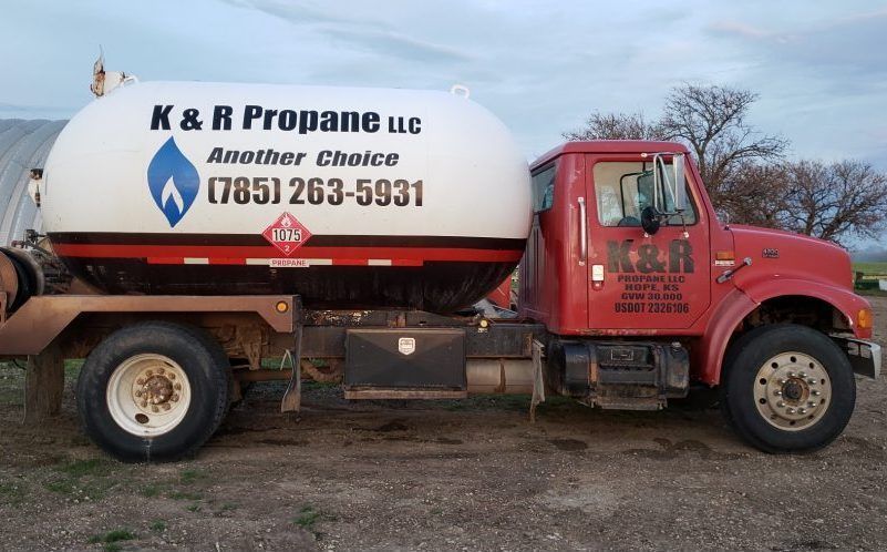 Red tanker truck with K&R Propane LLC logo parked outdoors on a dirt lot.