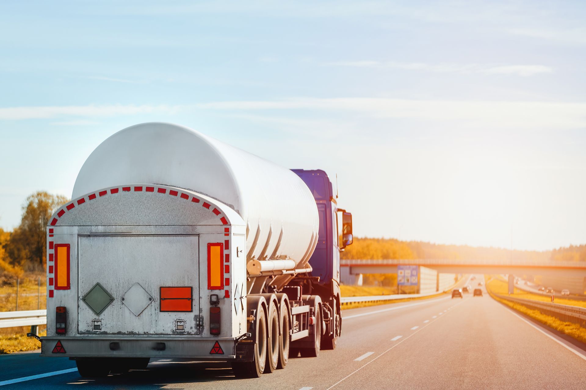 White tanker truck driving on a sunlit highway at dawn or dusk