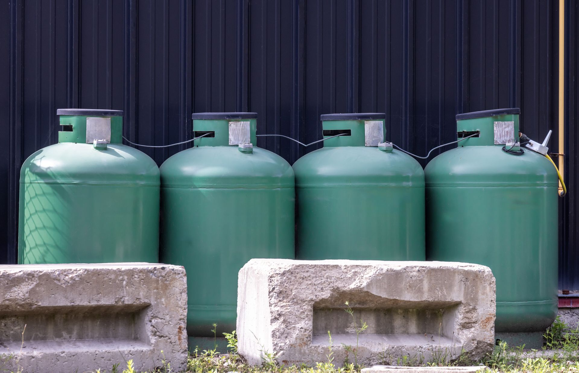 Four green gas tanks behind concrete blocks in front of a dark curtain