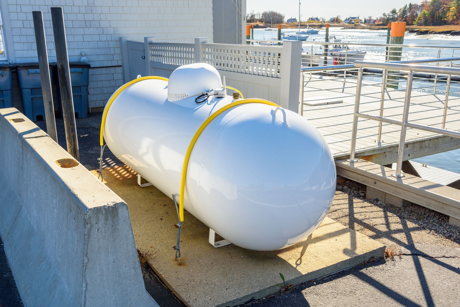 Two white propane tanks on a rooftop, secured with yellow straps near a railing and concrete wall.