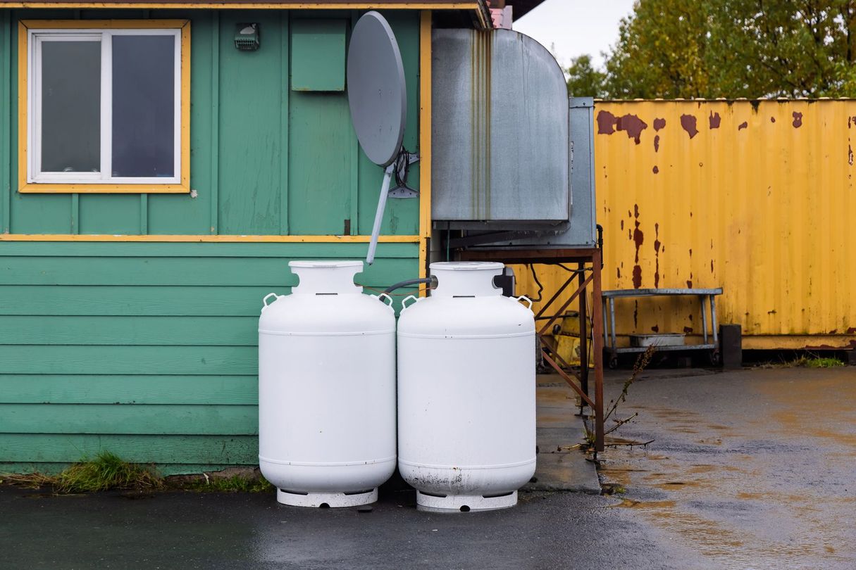 Two white propane tanks beside a green building and yellow fence on wet pavement