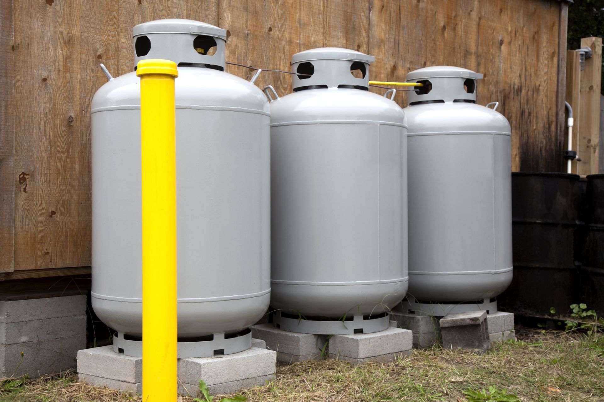 Three white propane tanks beside a wooden fence, with a yellow post in the foreground.