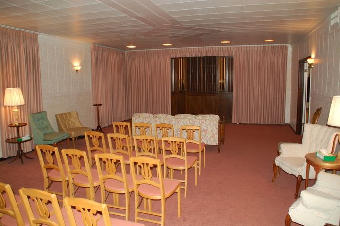 Empty banquet hall with rows of wooden chairs, tables, and beige curtains under warm lighting