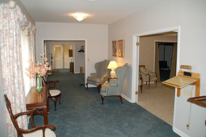 Carpeted living room with armchairs, lamp, side table, and open doorway to a dining area