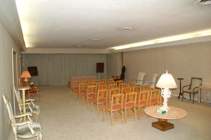 Empty beige conference room with rows of orange chairs, side tables, and lamps under recessed ceiling lights