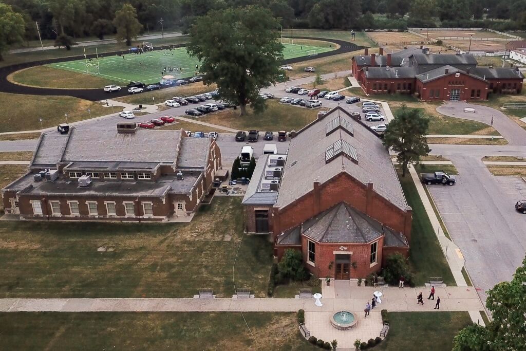 Aerial view of a brick complex with parking lot, lawns, and a fountain