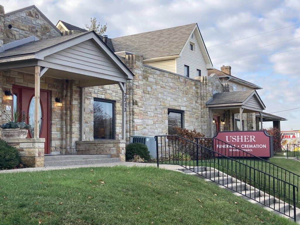 Stone church building with a covered entrance and a red “Usher” sign by the walkway