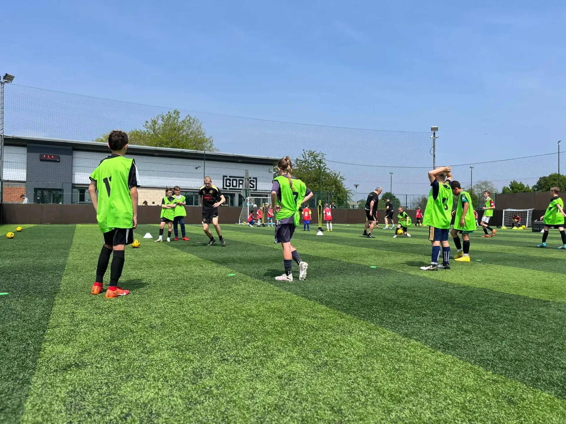 Children in neon green jerseys playing soccer on an outdoor turf field under a blue sky