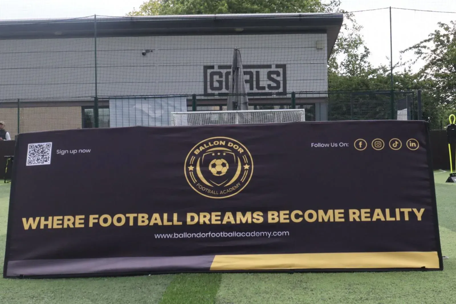 Black football banner on a field reads “WHERE FOOTBALL DREAMS BECOME REALITY.”