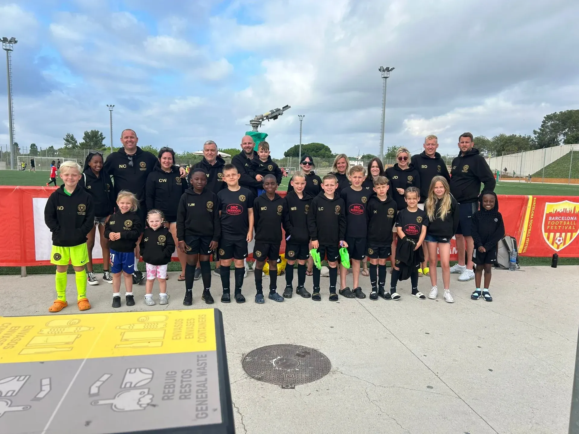 Youth soccer team posing on a field with coaches, wearing black uniforms and neon socks, holding a trophy.